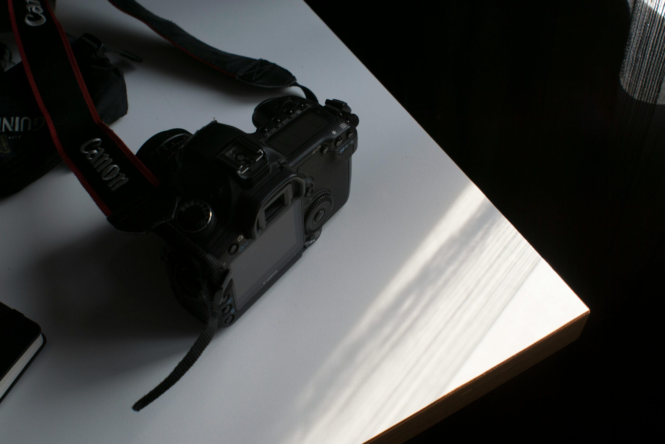 A DSLR camera with a strap on a table, illuminated by natural light.